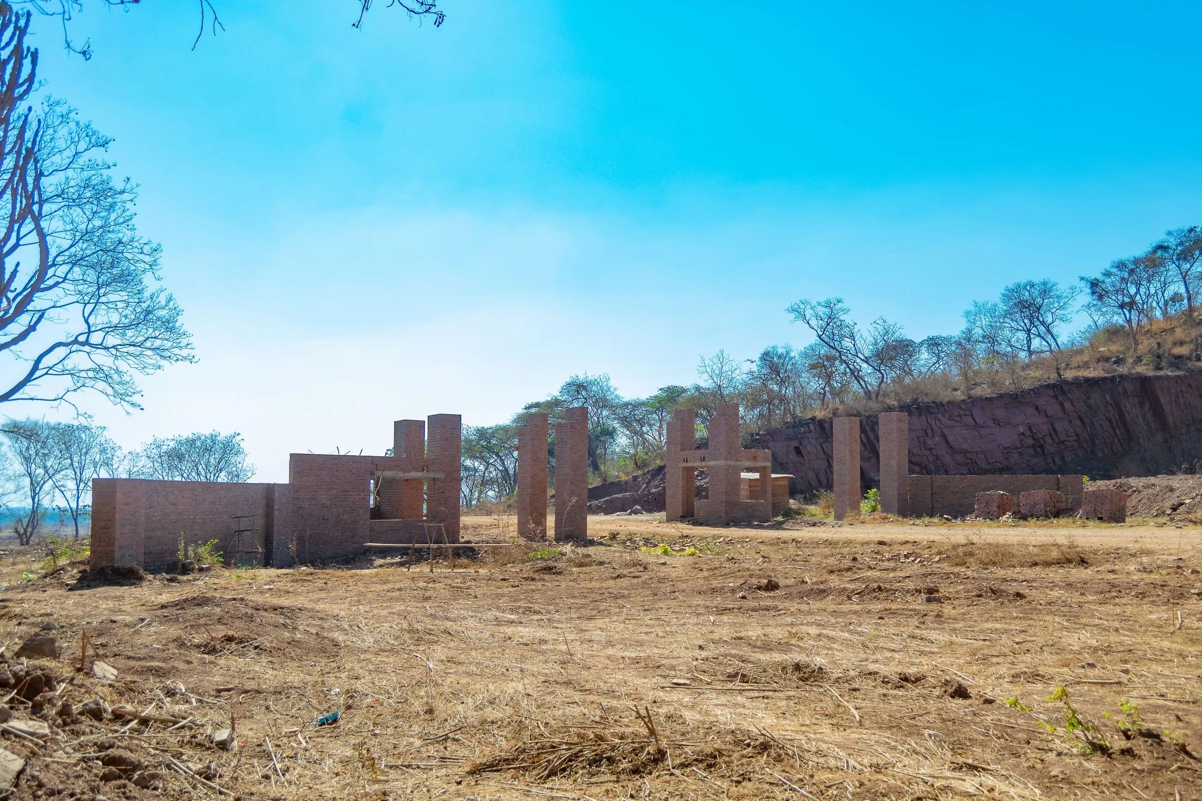 Brick walls and piers of the estate entrance buildings standing without roofs, on cleared ground below a wooded ridge